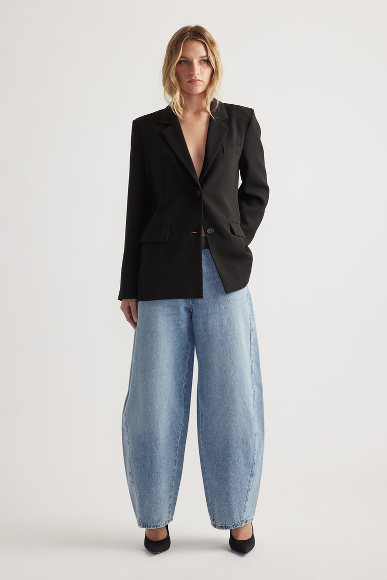 Woman wearing a sleek black tailored blazer paired with light-wash wide-leg denim jeans and black heels