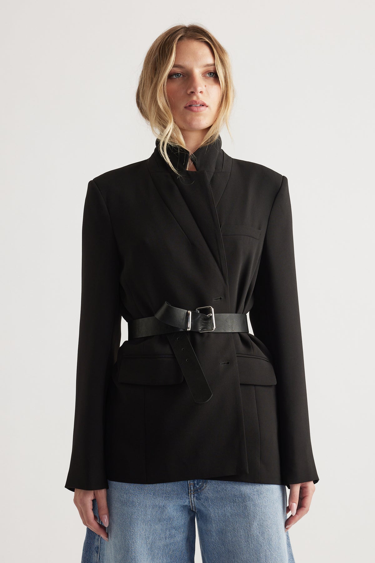 Woman wearing a black tailored blazer cinched with a black belt, styled with light wash loose jeans for a modern look