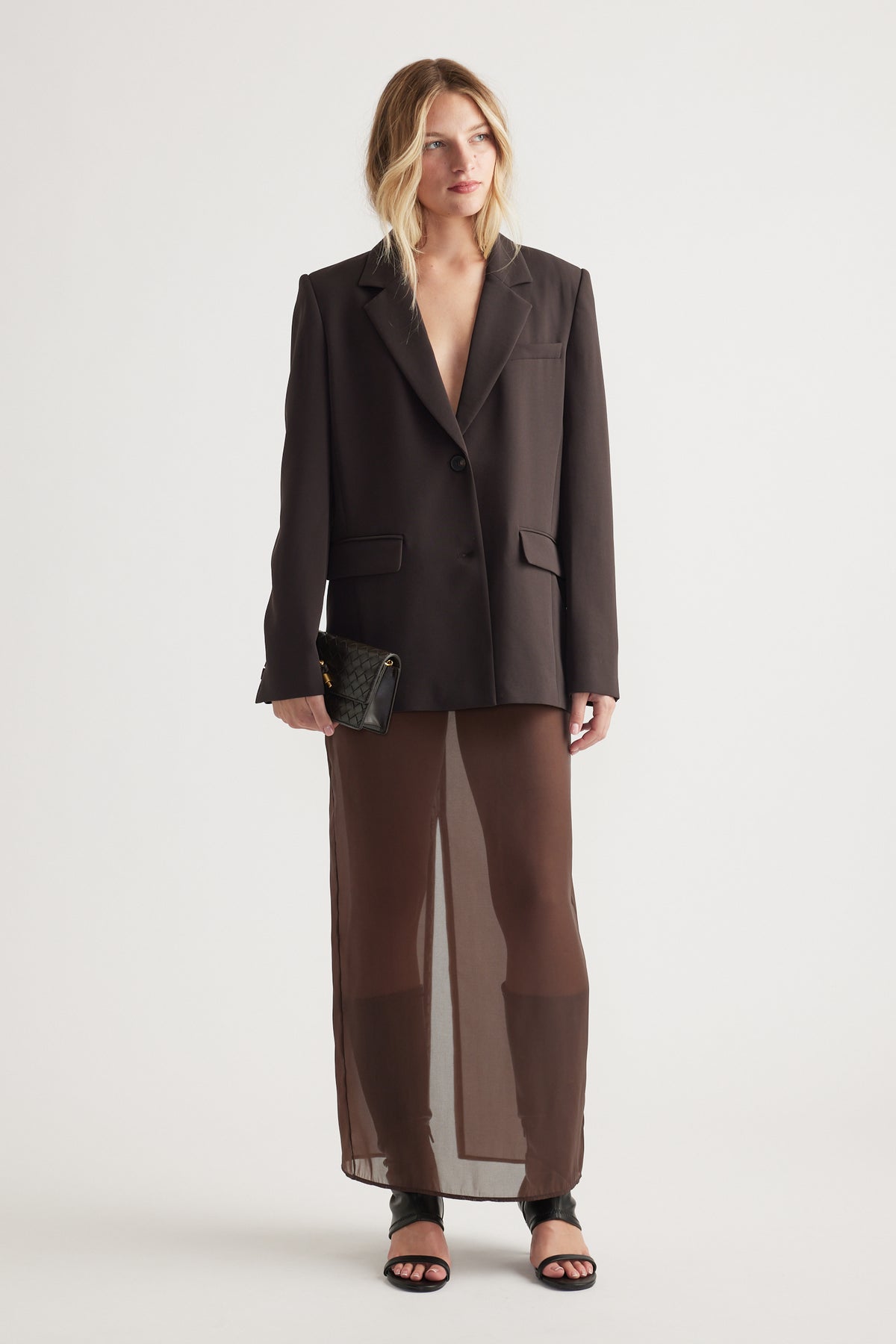 Woman wearing a chocolate brown tailored blazer paired with a sheer matching skirt and black heeled sandals