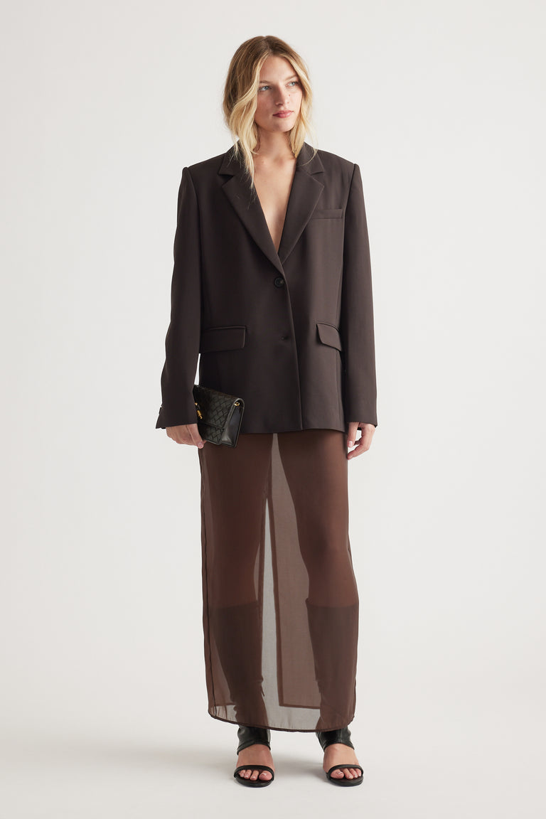 Woman wearing a chocolate brown tailored blazer paired with a sheer matching skirt and black heeled sandals