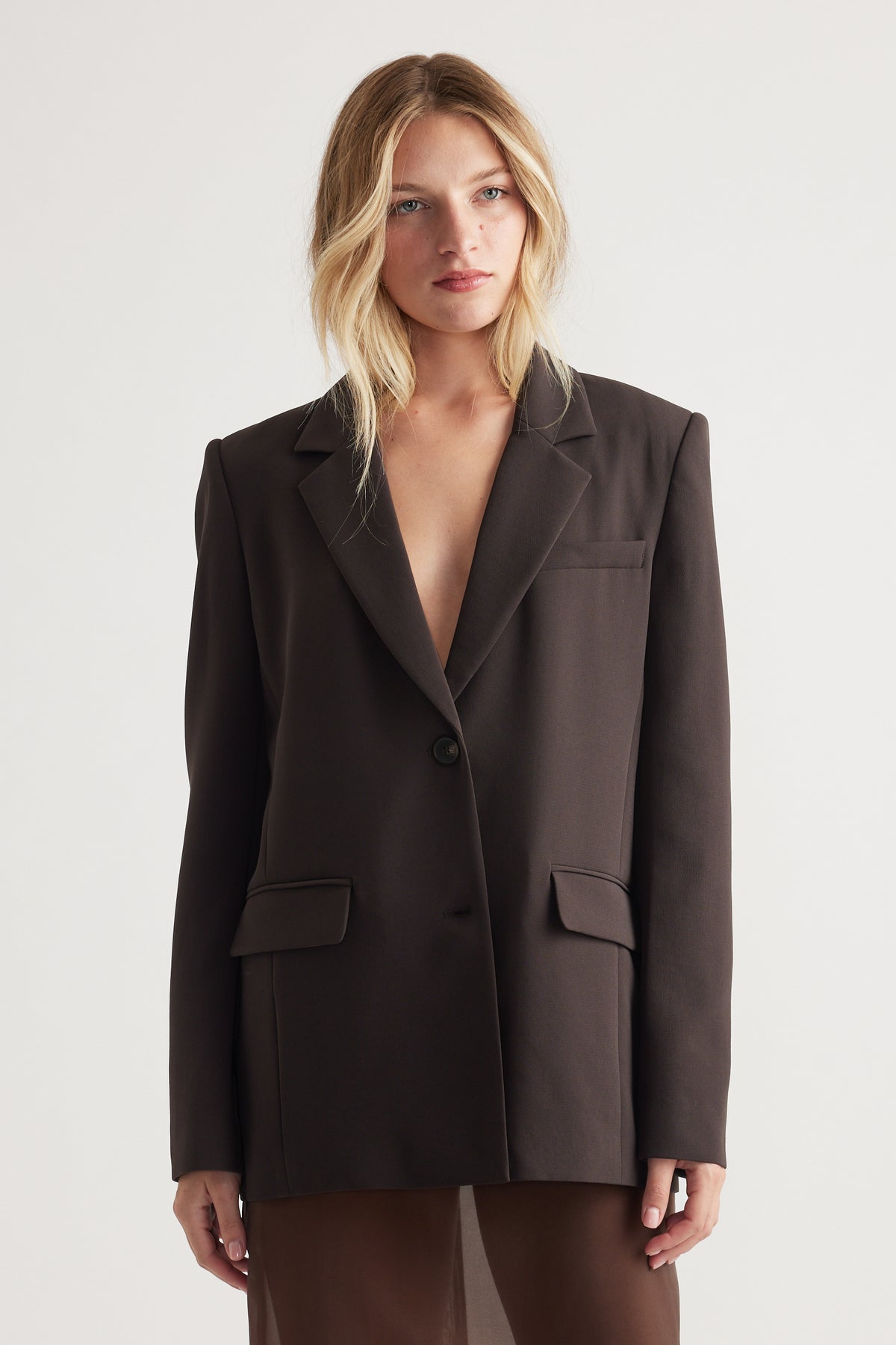 Woman wearing a dark tailored blazer with a single button, structured shoulders, and flap pockets for a sleek, polished look