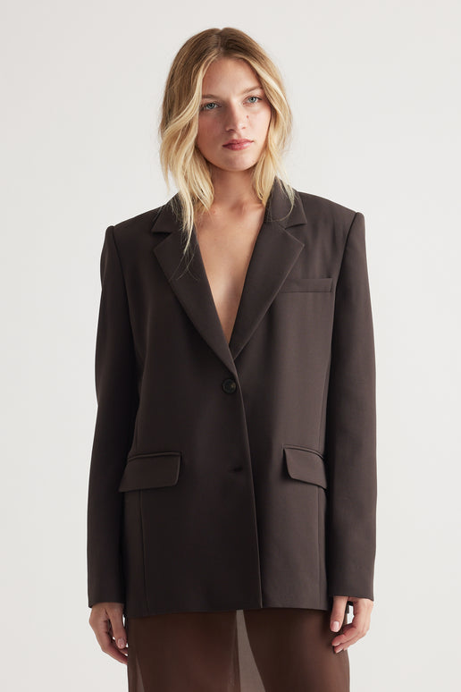 Woman wearing a dark tailored blazer with a single button, structured shoulders, and flap pockets for a sleek, polished look