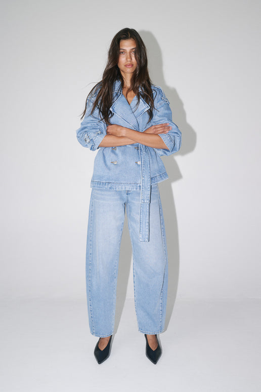 Woman wearing light wash high-rise barrel leg jeans with a belted denim jacket and black pointed heels