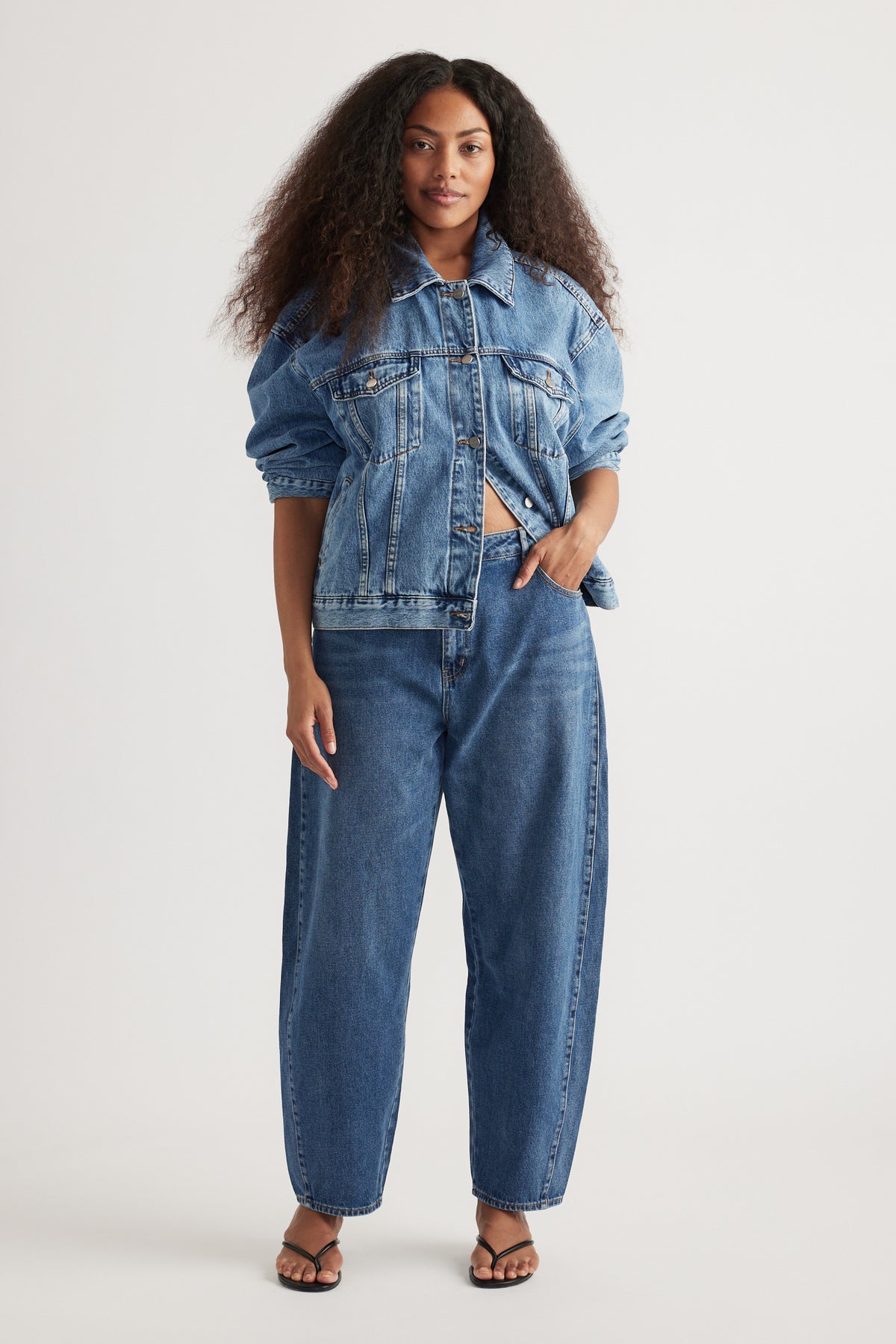 Woman wearing a denim jacket with high rise blue barrel leg jeans and strappy sandals