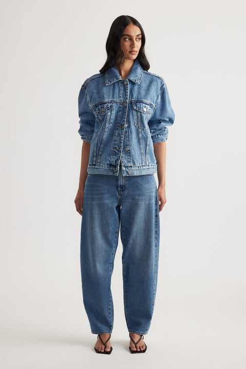 Woman wearing a relaxed fit blue denim jacket paired with high-rise tapered jeans and black open-toe sandals