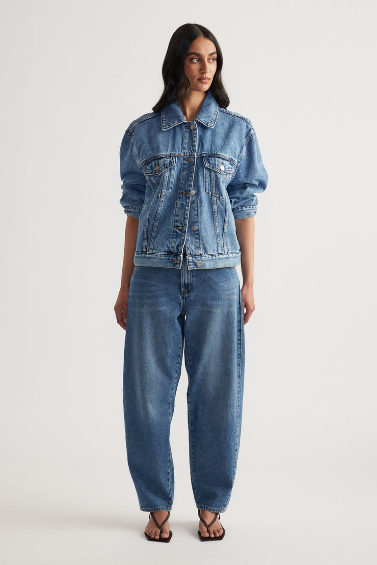 Woman wearing a relaxed fit blue denim jacket paired with high-rise tapered jeans and black open-toe sandals