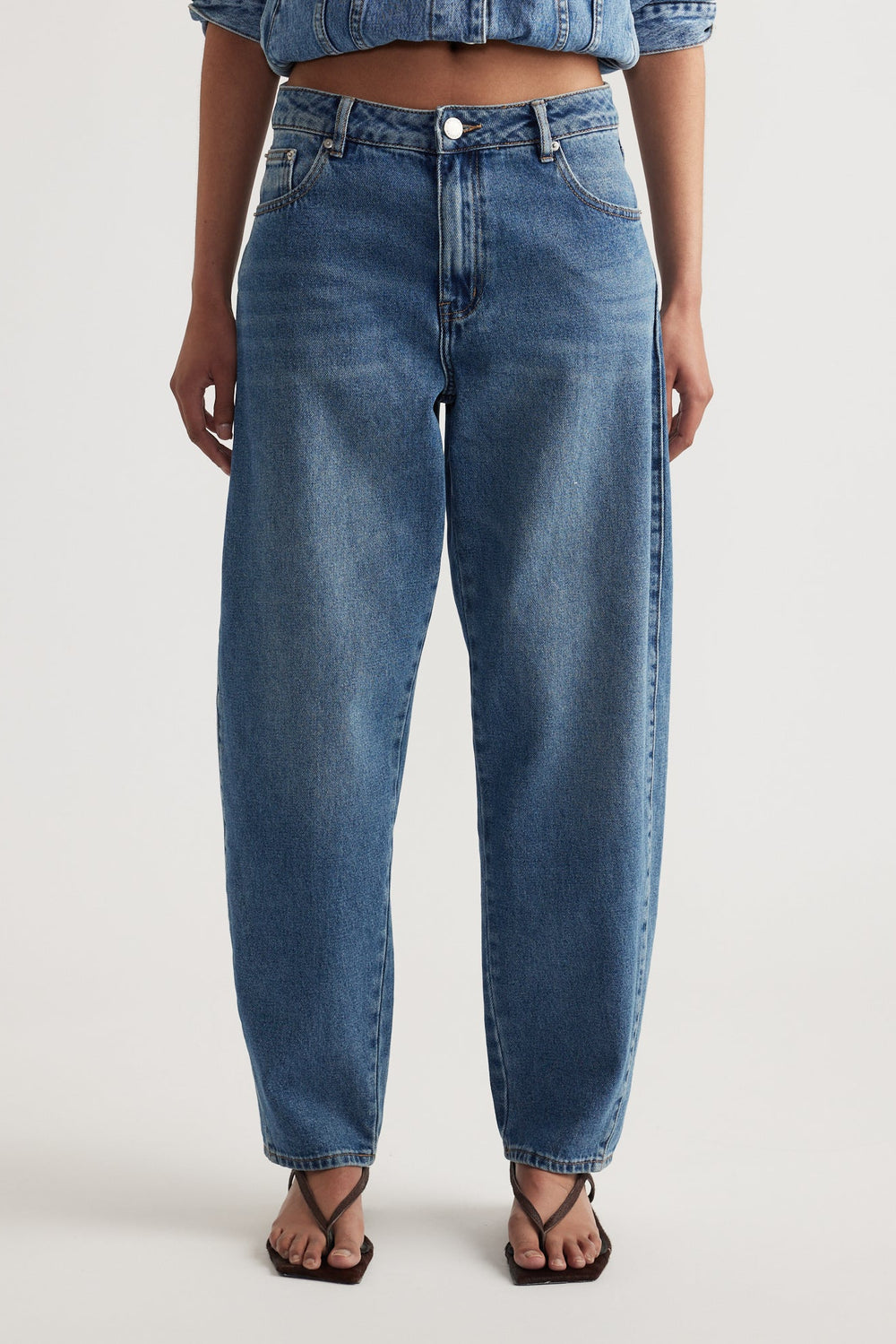 High-rise rigid denim jeans with a tapered ankle and relaxed barrel leg silhouette styled with square-toe sandals
