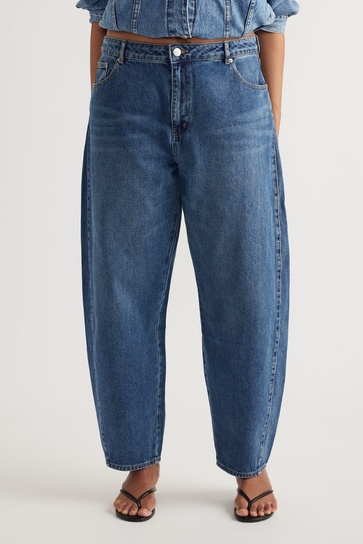 Woman wearing high rise blue barrel leg jeans with a curved silhouette and tapered ankles