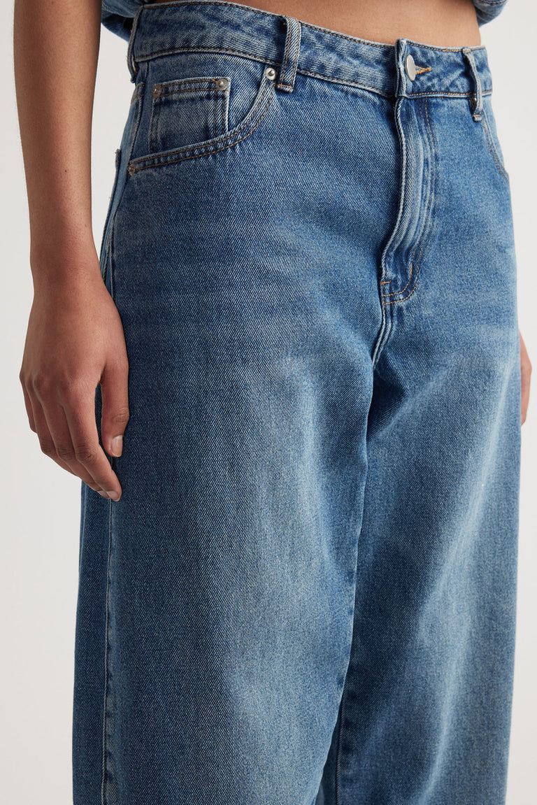 Close-up of a pair of high-rise blue denim jeans with a fitted waist and barrel leg silhouette.