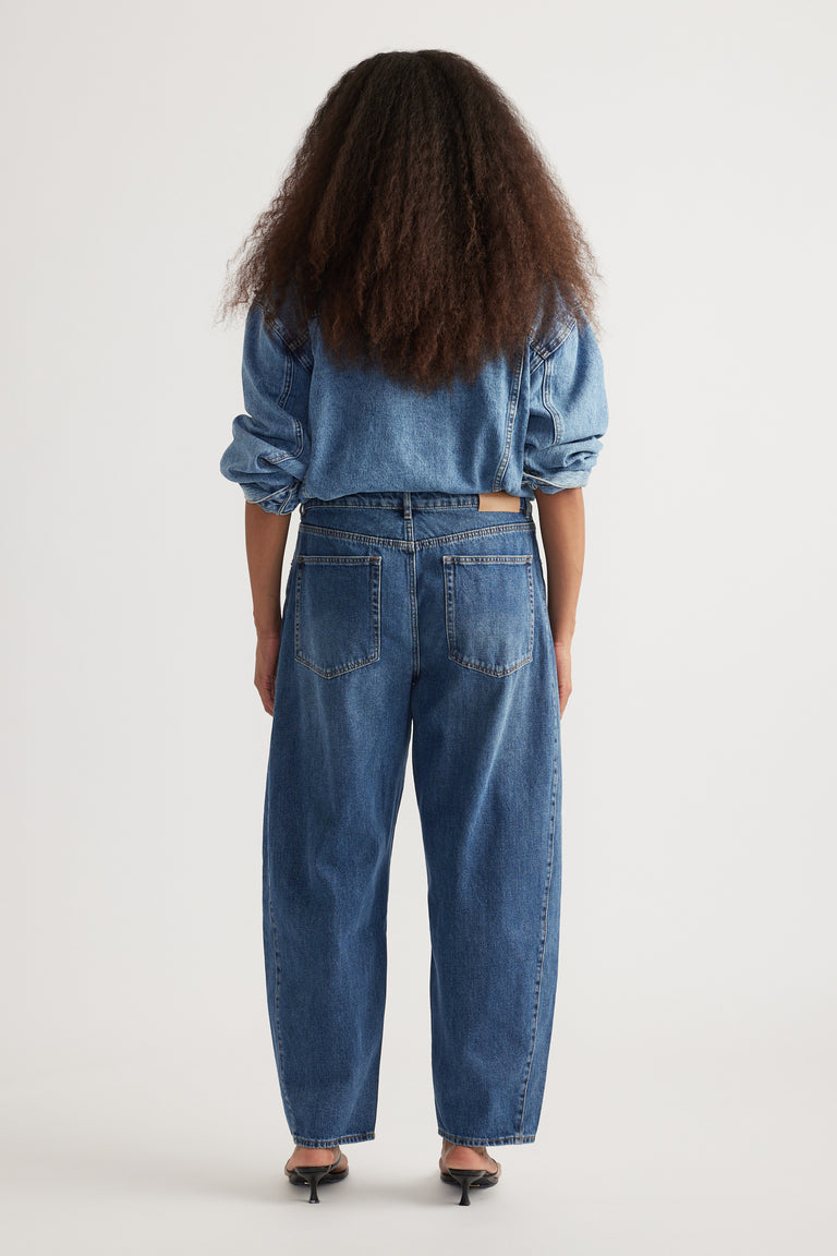 Woman wearing a denim shirt with high rise blue barrel leg jeans and tapered ankles, viewed from behind