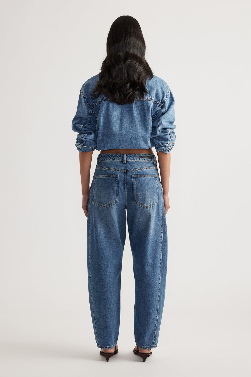 Woman seen from behind wearing high-rise blue denim barrel leg jeans and a cropped denim jacket with rolled sleeves