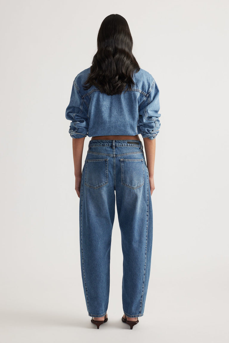 Woman seen from behind wearing high-rise blue denim barrel leg jeans and a cropped denim jacket with rolled sleeves