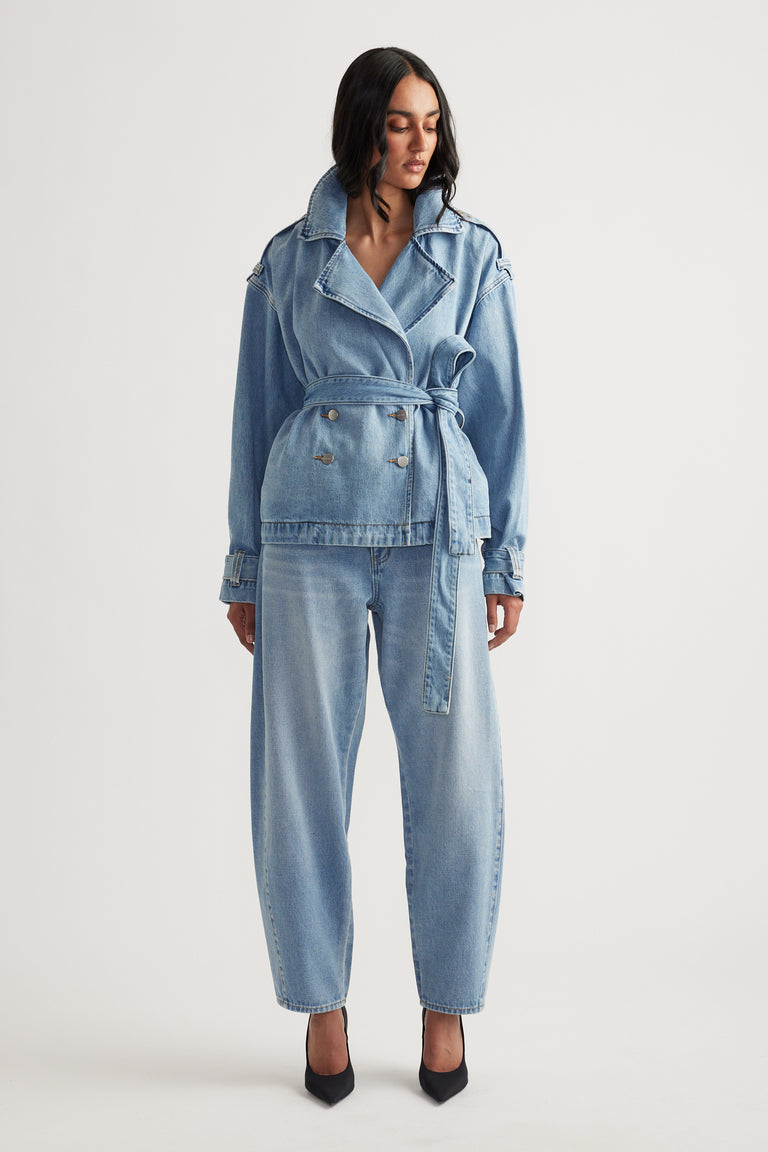Woman wearing light blue belted denim jacket paired with relaxed fit barrel leg jeans and black pointed heels