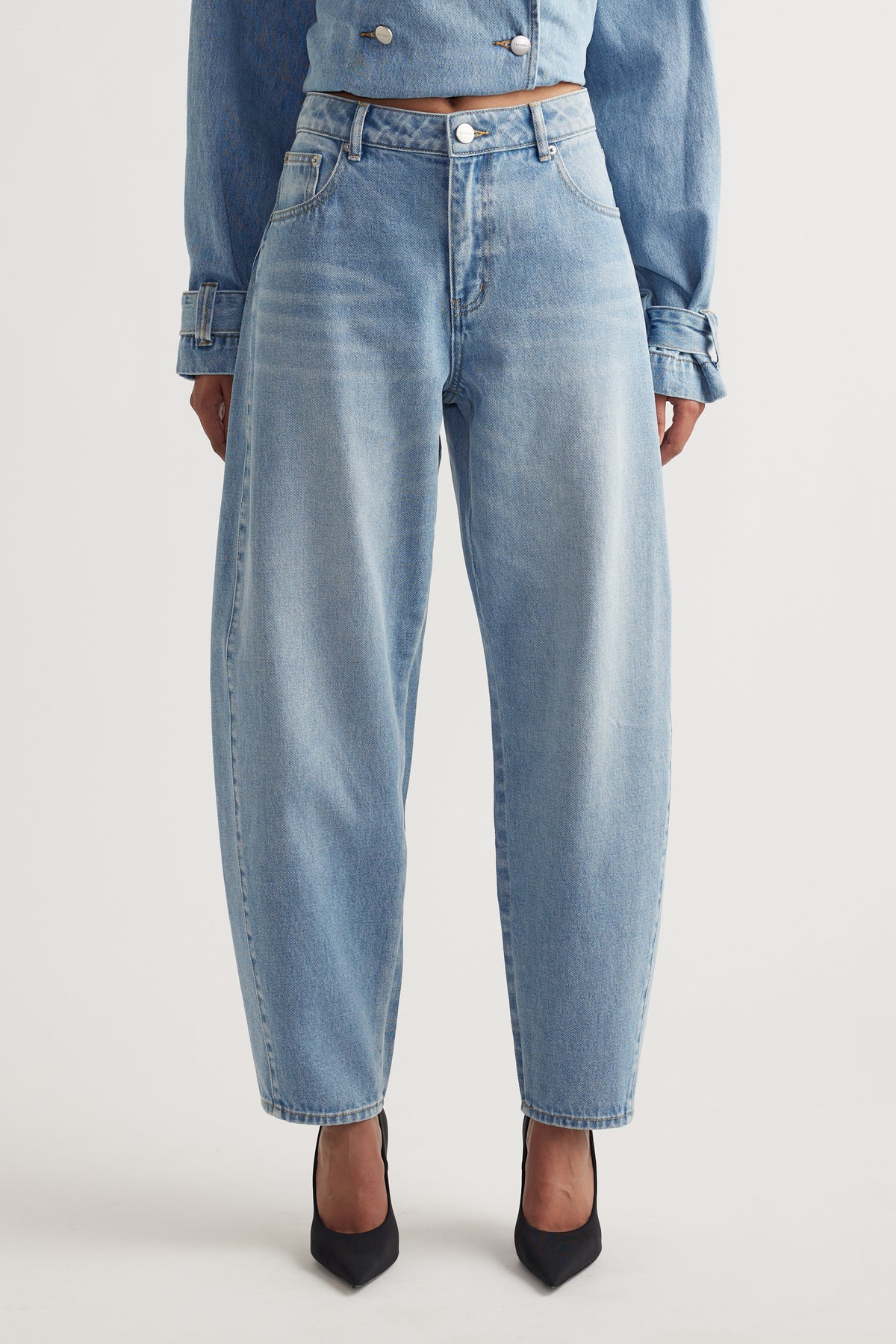 Light wash barrel leg jeans styled with black pointed heels and a matching cropped denim jacket