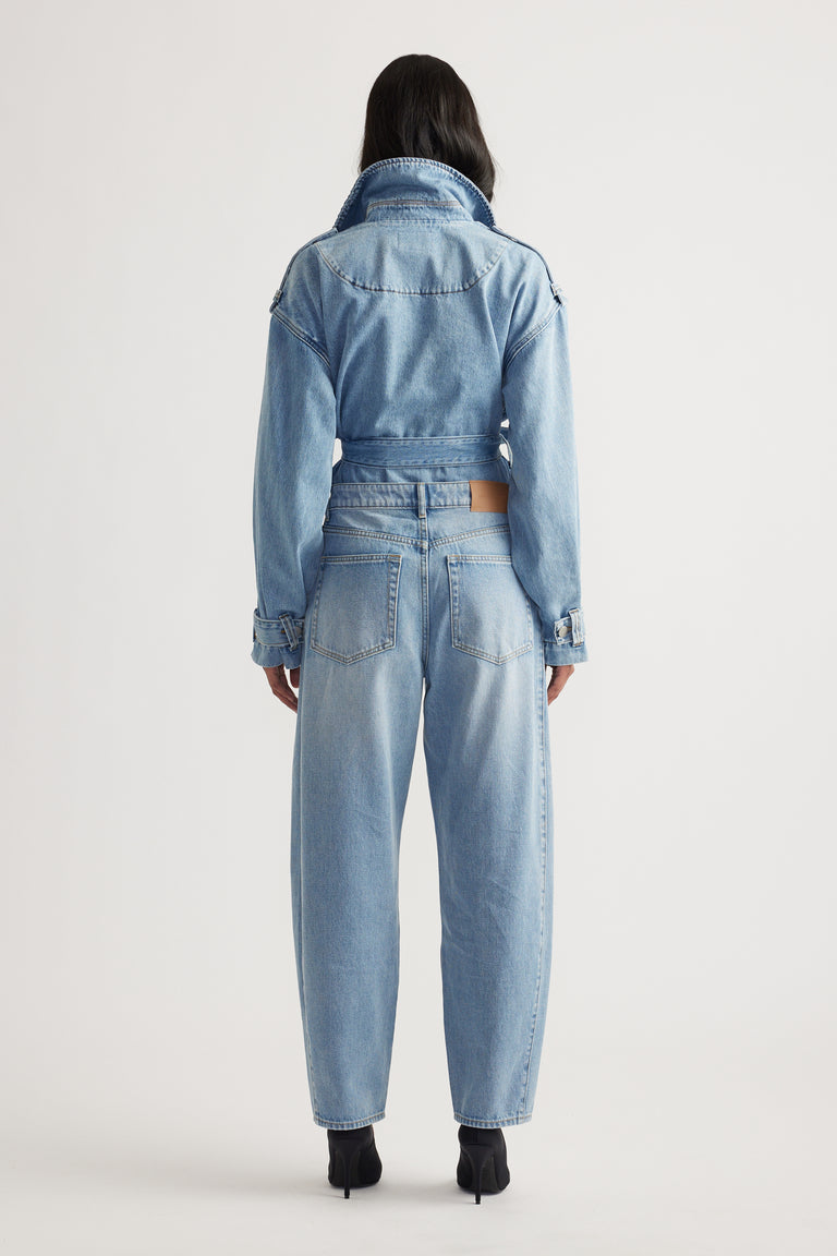 Woman shown from behind wearing light indigo cropped denim jacket with high-waisted barrel leg jeans and black heels