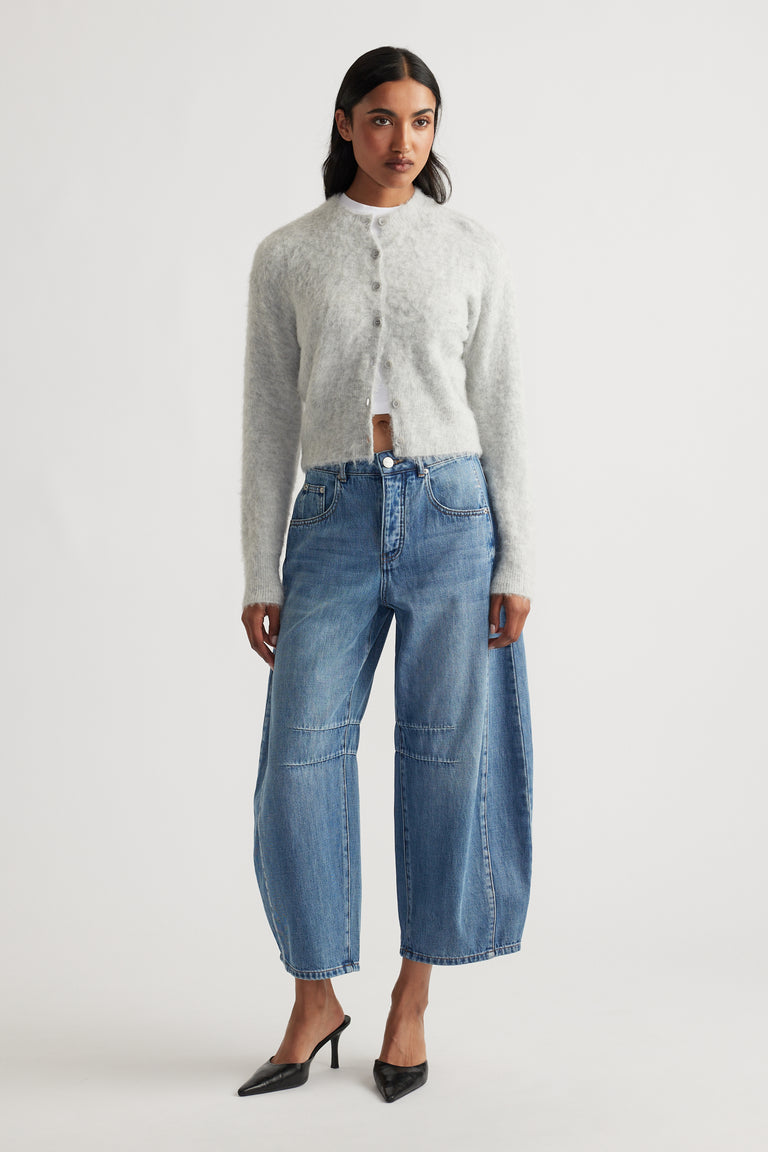 Model wearing a soft light grey fluffy cardigan over a white top paired with relaxed wide-leg blue denim jeans and black pointed heels.