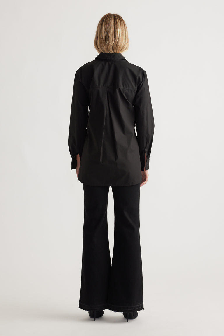 Back view of a woman wearing a sleek black tailored shirt with long sleeves paired with flared black pants and heels