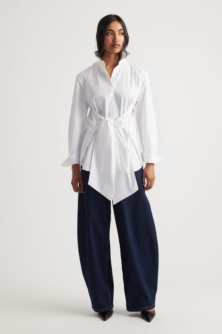 Woman wearing a white tie-front shirt paired with wide-leg dark denim jeans and black pointed shoes for a modern look