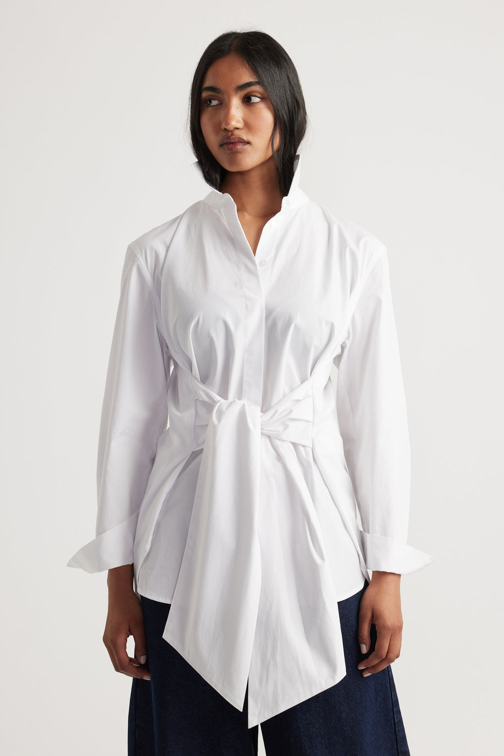 Woman wearing a white long-sleeve shirt with a tied waist detail paired with dark wide-leg pants.