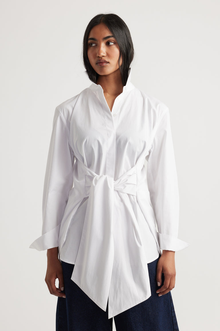 Woman wearing a white long-sleeve shirt with a tied waist detail paired with dark wide-leg pants.