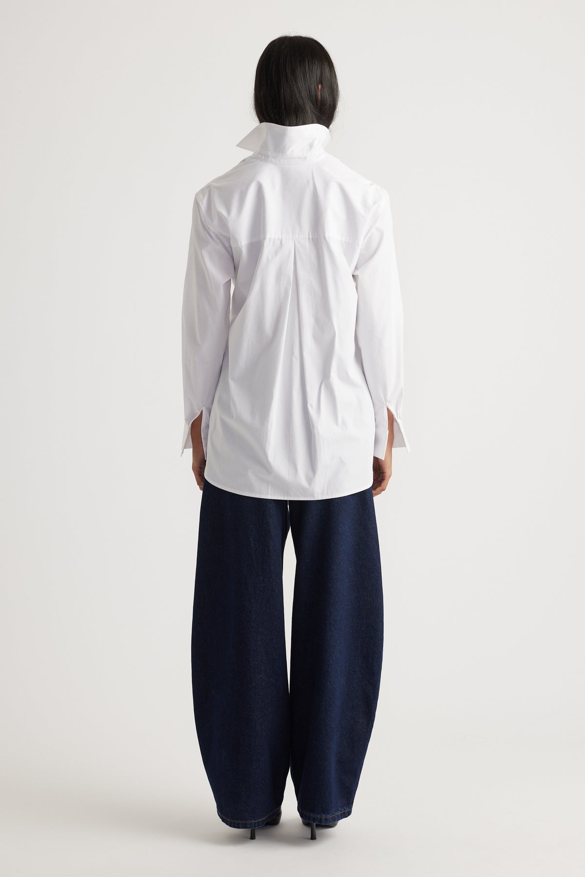 Back view of a woman wearing a crisp white tie-front shirt paired with wide-leg dark denim jeans and heels.