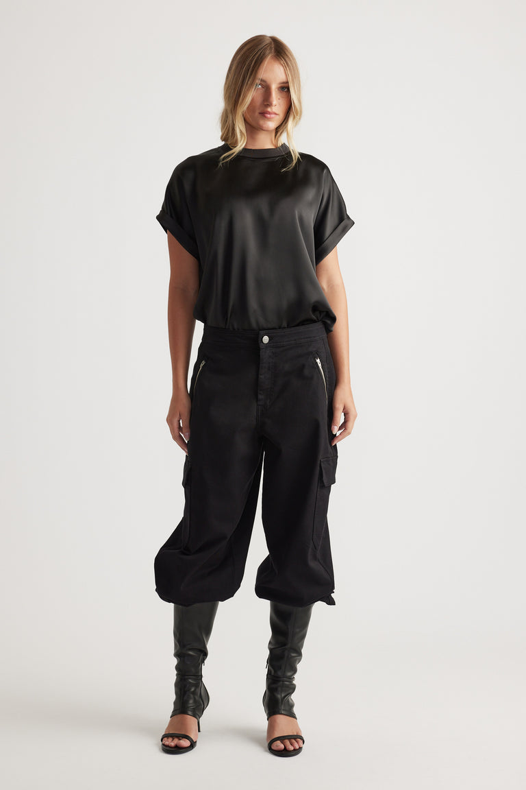 Woman wearing AnnMaree Satin Tee in black styled with relaxed cargo pants and black open-toe heels for modern casual look.