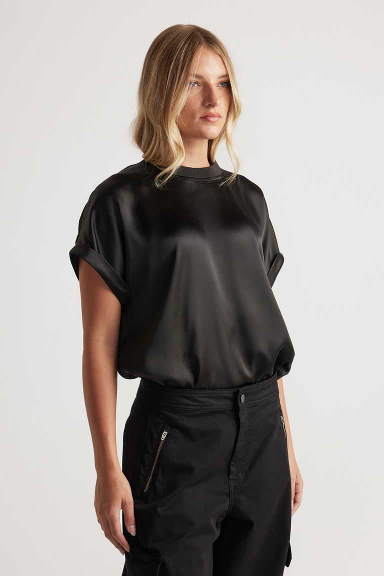 Woman wearing AnnMaree Satin Tee in black with rolled sleeves styled with relaxed black pants for a sleek look
