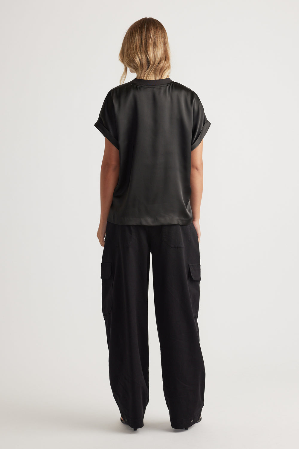 Woman seen from behind wearing AnnMaree Satin Tee in black paired with loose black cargo pants for a relaxed look