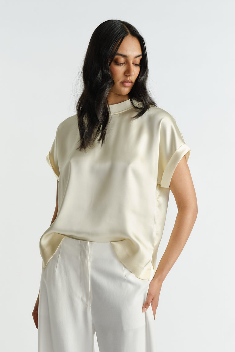 Woman wearing a relaxed fit satin tee in soft buttery cream paired with wide-leg white pants for a polished look