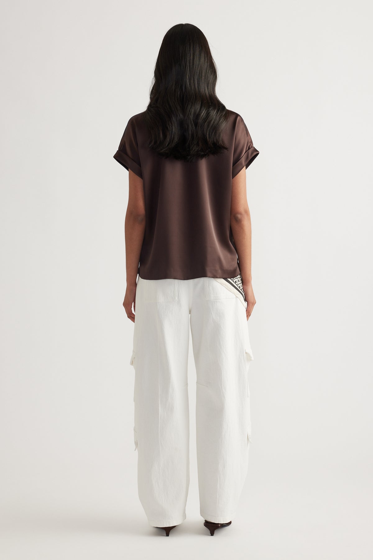 Model viewed from behind wearing a brown satin short sleeve tee with white wide leg pants