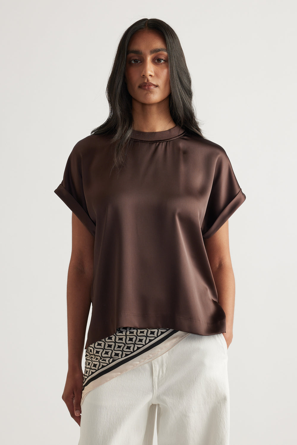 Woman wearing a brown satin short sleeve top with white pants and a patterned waist detail