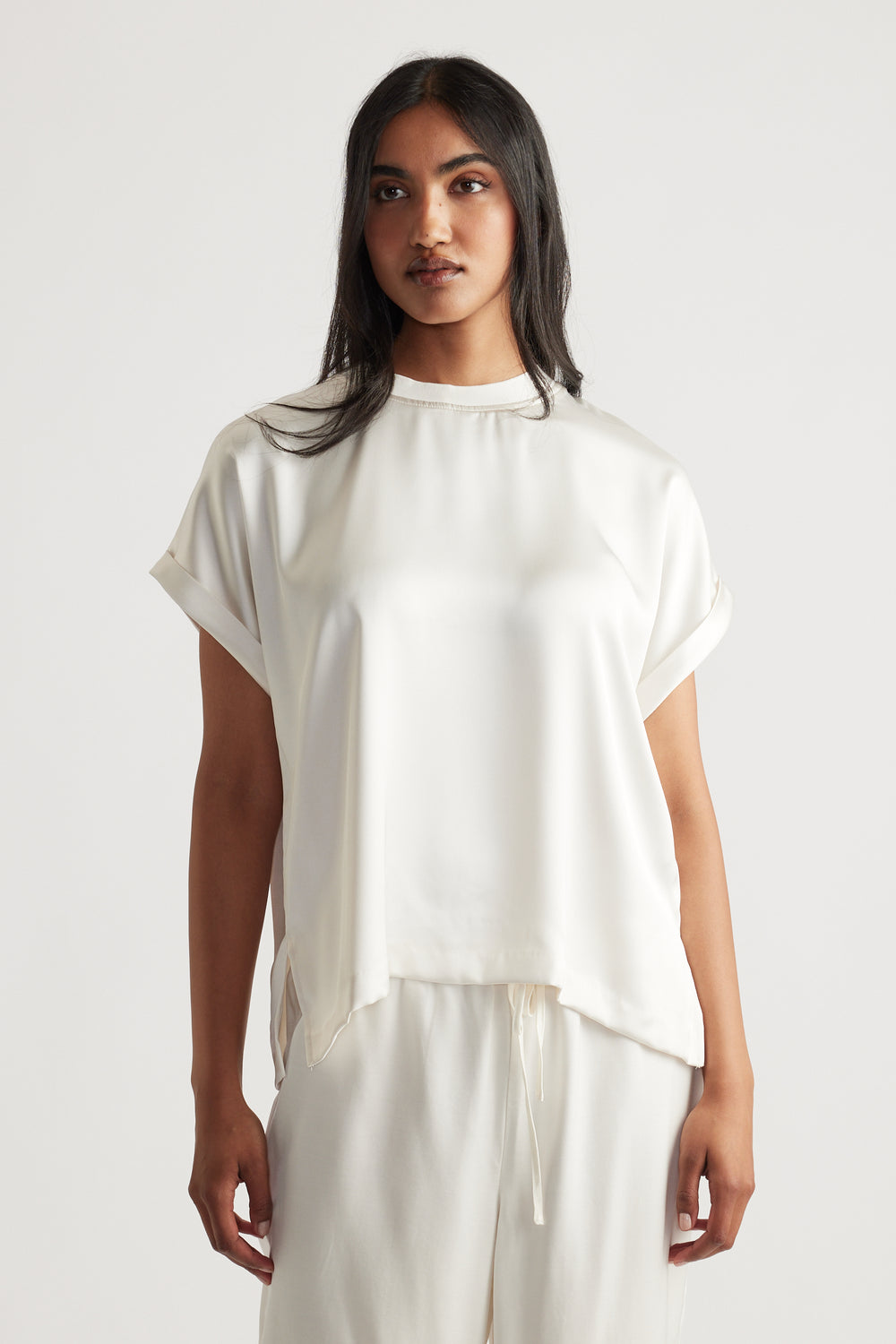 Woman wearing an elegant cream satin tee with rolled short sleeves and relaxed drawstring pants for a refined casual look
