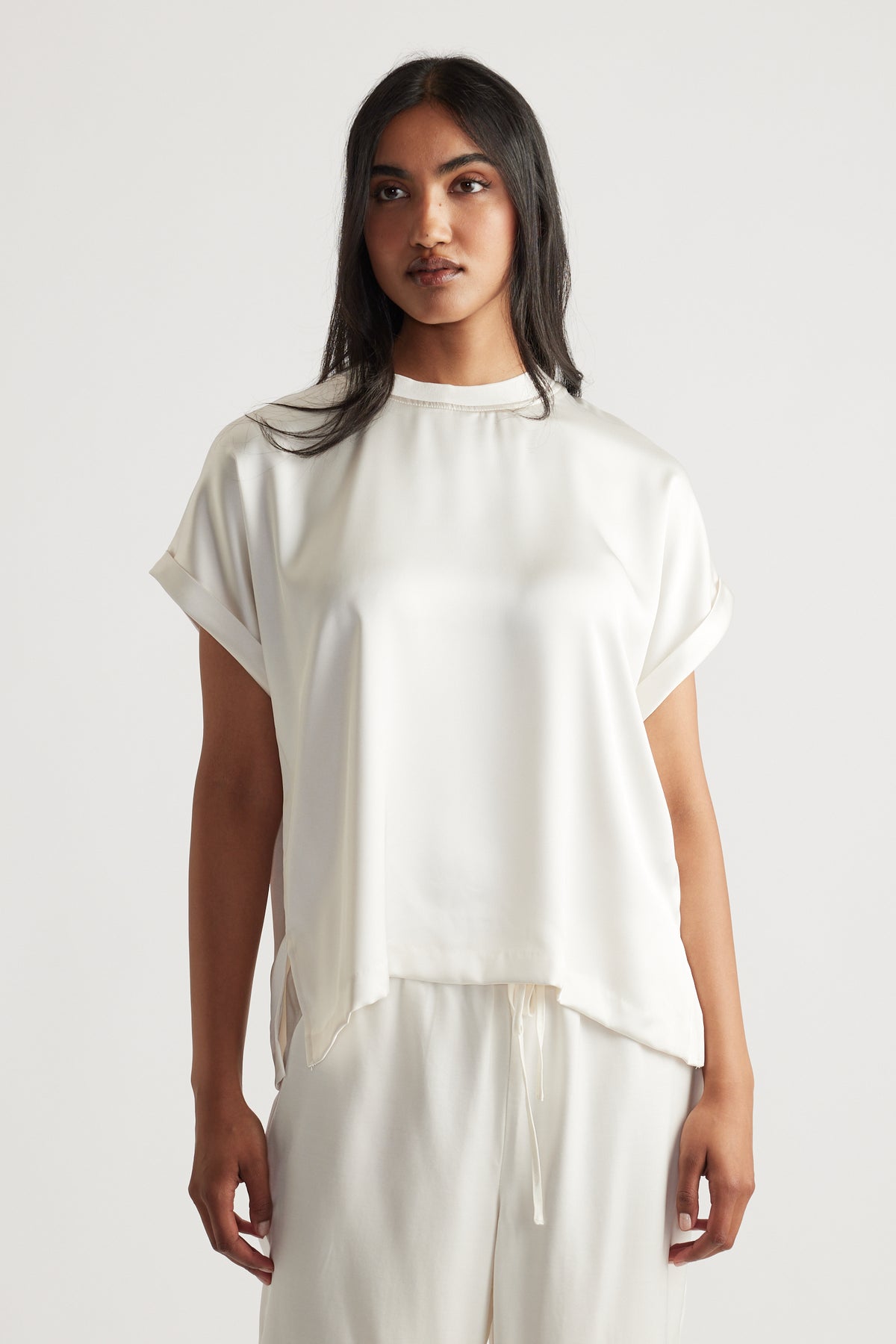 Woman wearing an elegant cream satin tee with rolled short sleeves and relaxed drawstring pants for a refined casual look