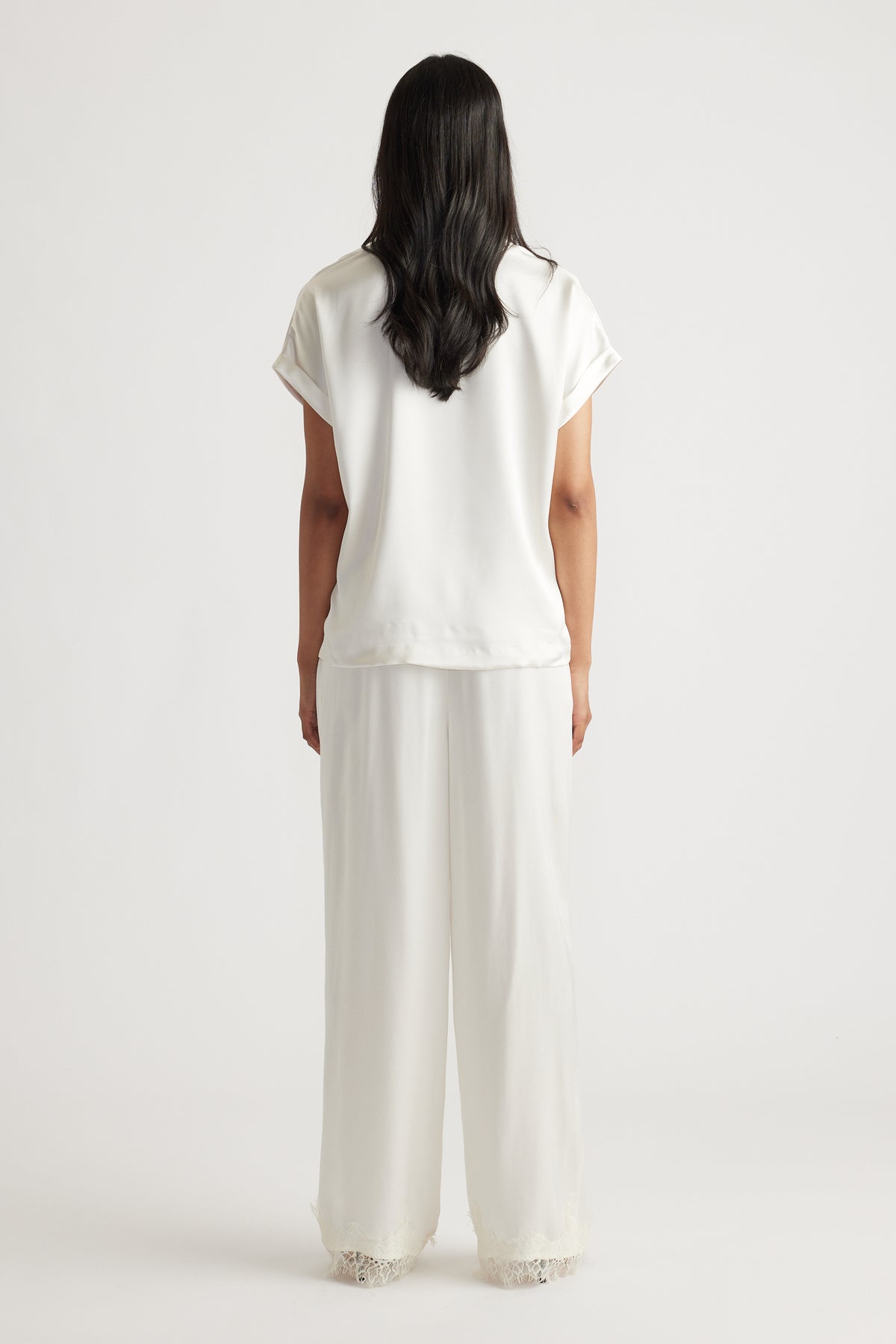 Woman wearing a relaxed white satin tee paired with wide-leg pants featuring lace trim for an elegant casual look