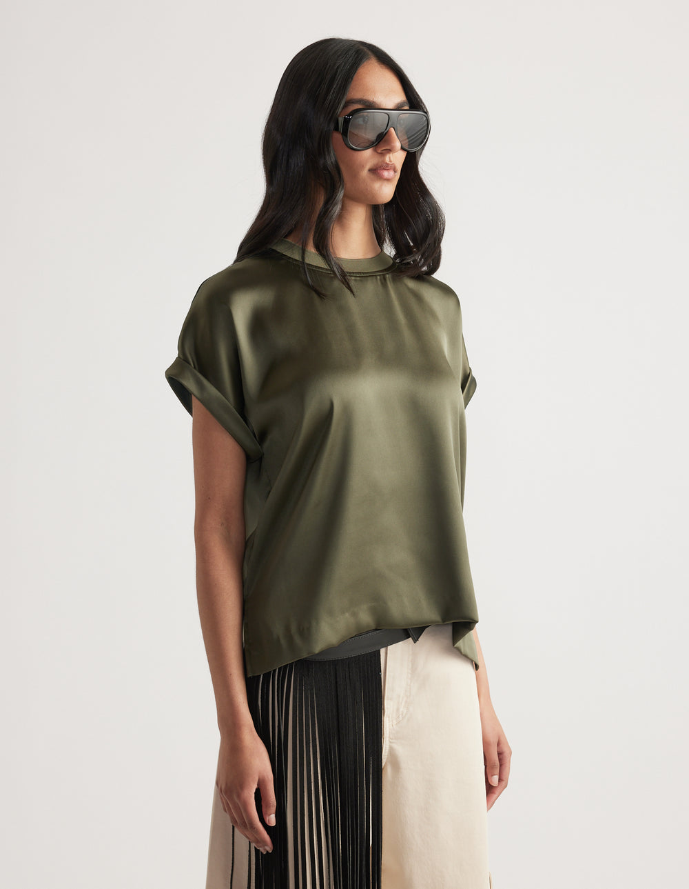 Woman wearing an olive green satin tee with rolled sleeves paired with pleated black and cream wide-leg pants and sunglasses