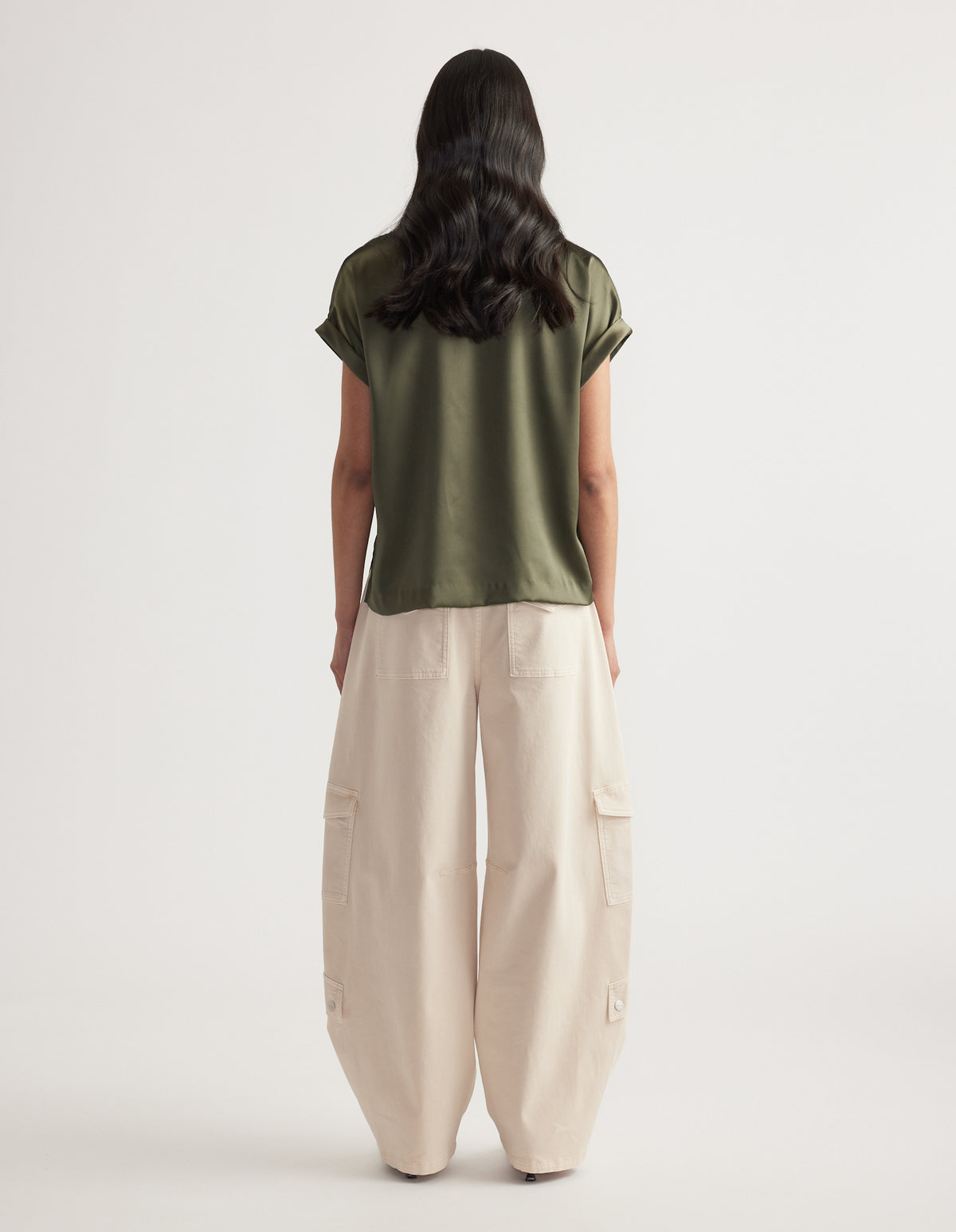 Woman wearing an olive satin short sleeve top paired with loose cream wide-leg cargo pants against a neutral backdrop