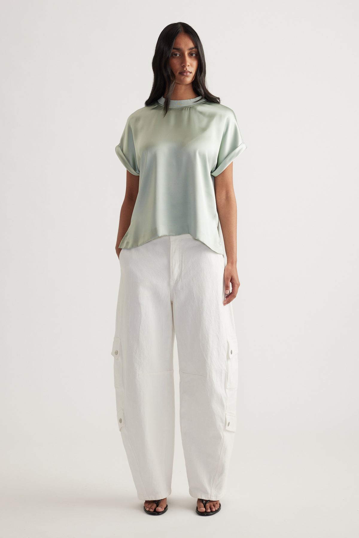 Woman wearing a sage green satin short sleeve tee with white cargo pants and sandals