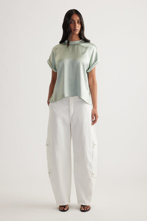 Woman wearing a sage green satin short sleeve tee with white cargo pants and sandals