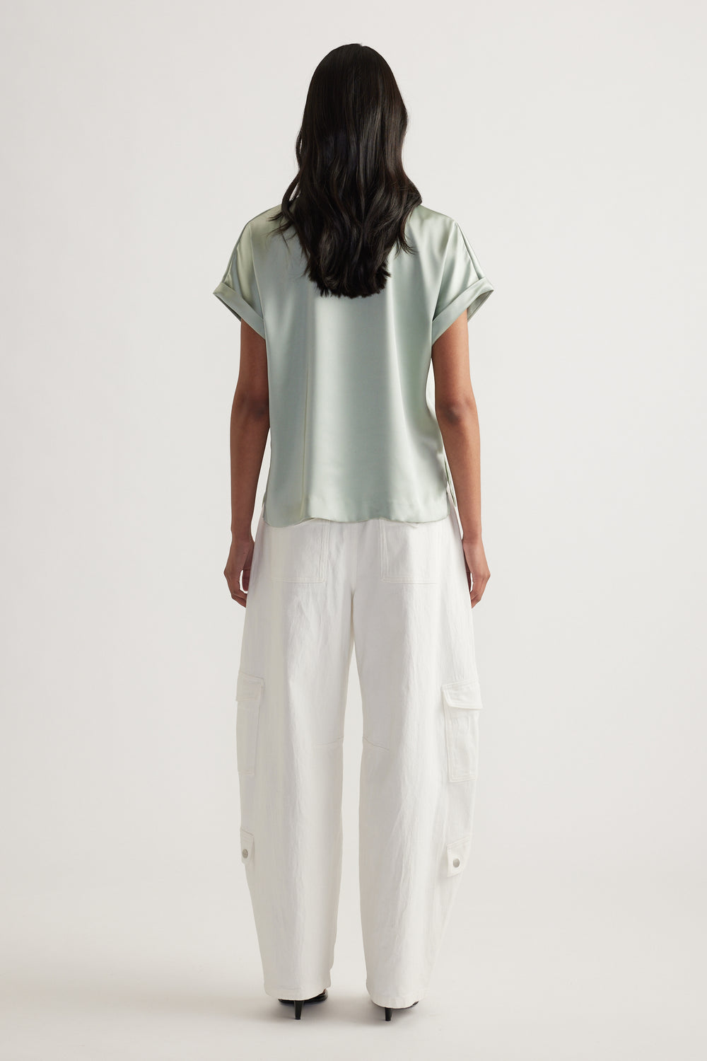 Woman viewed from behind wearing a sage satin short sleeve tee with white cargo pants