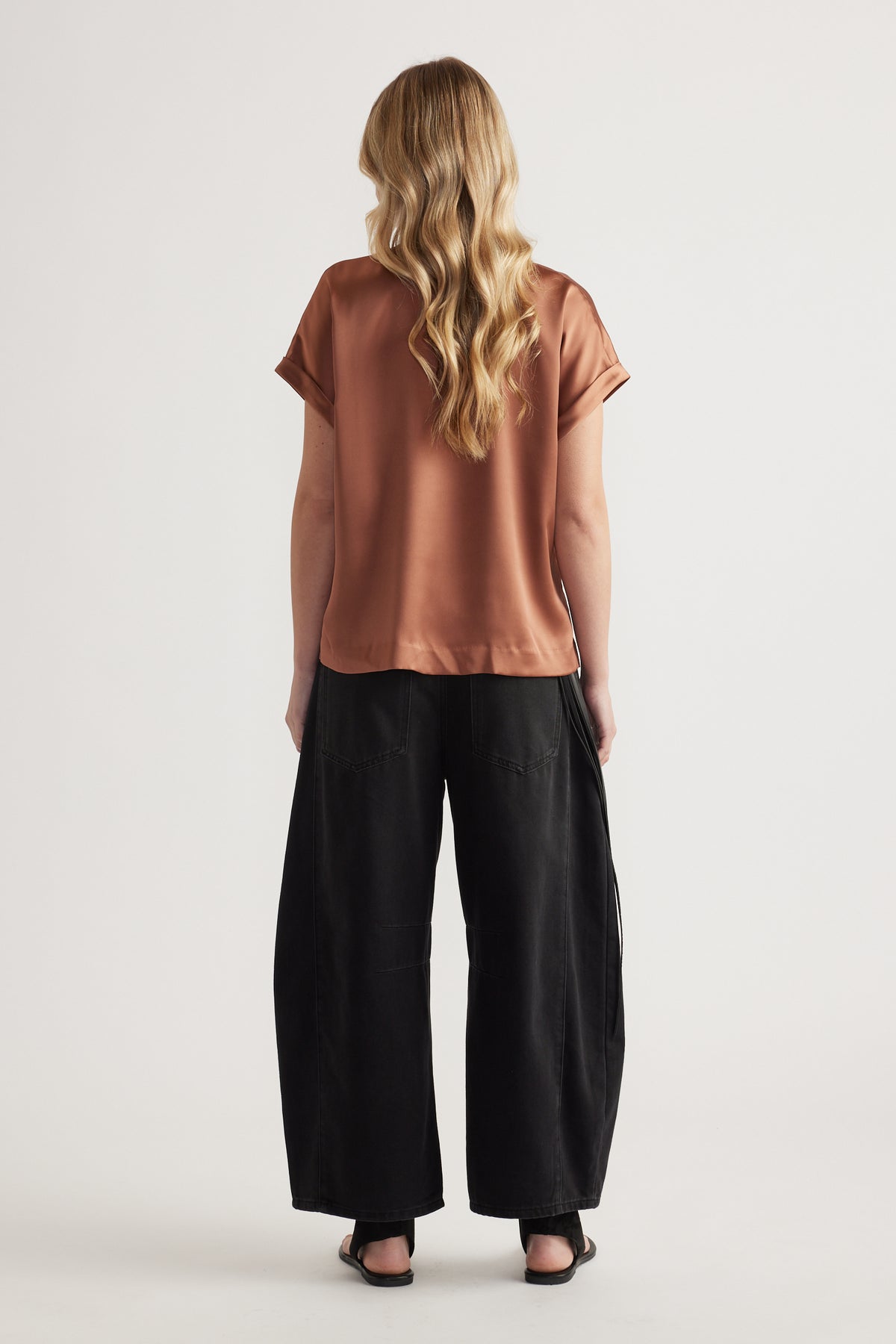 Woman seen from behind wearing a rust satin short sleeve tee with black wide-leg pants