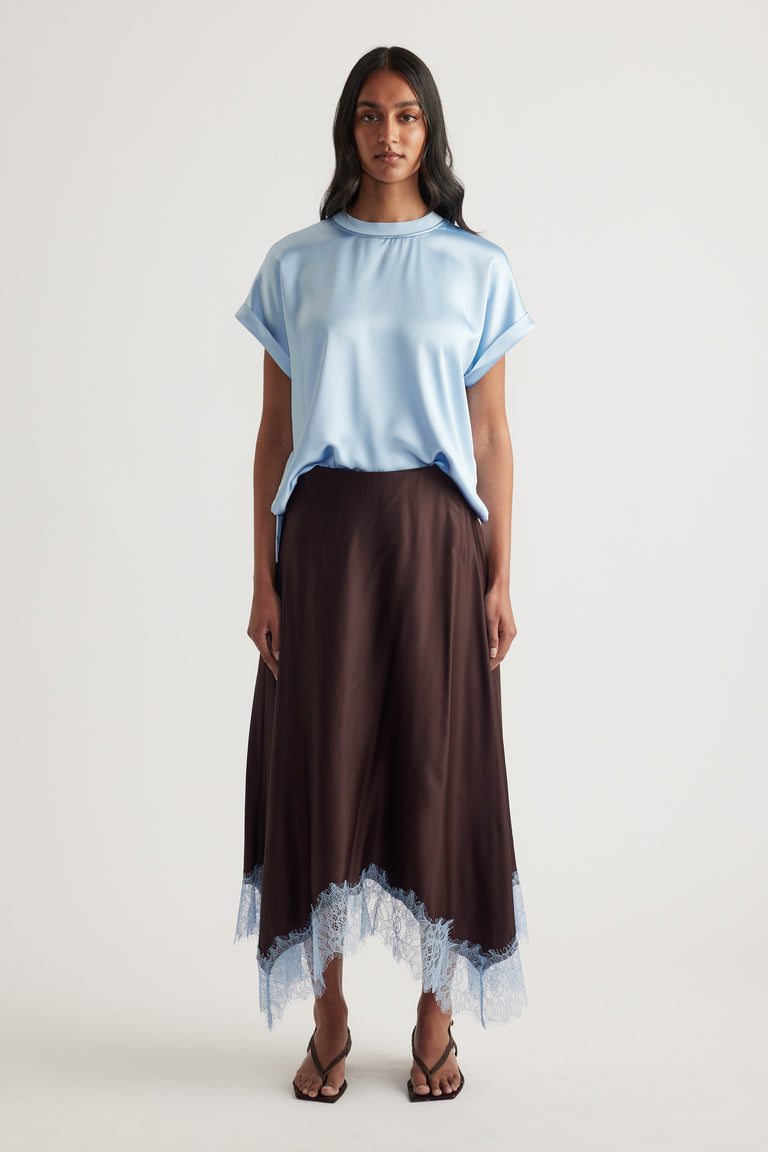 Model wearing a light blue satin tee with a relaxed fit and brown skirt with lace trim