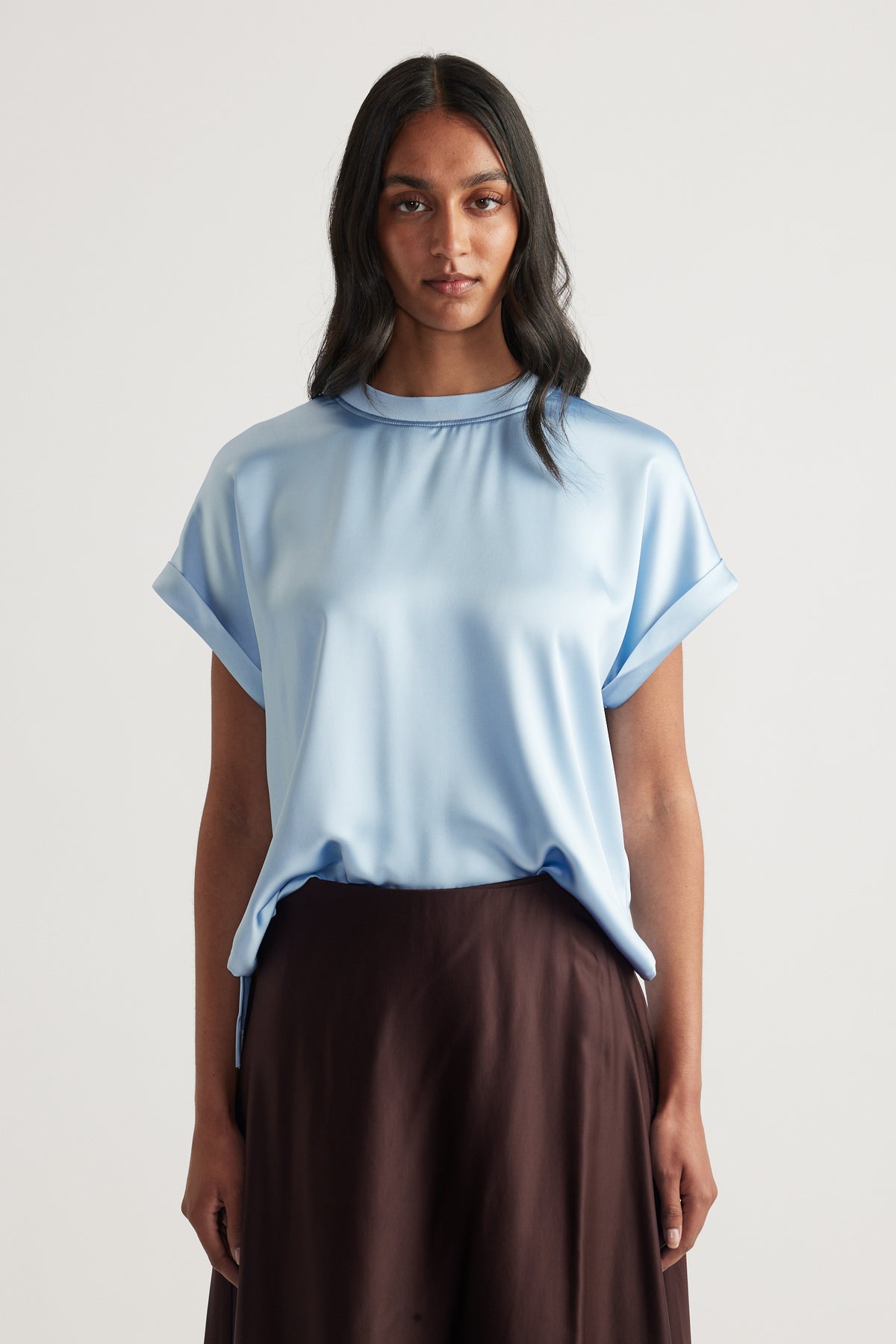 Model wearing a light blue satin tee with short sleeves and dark brown pants