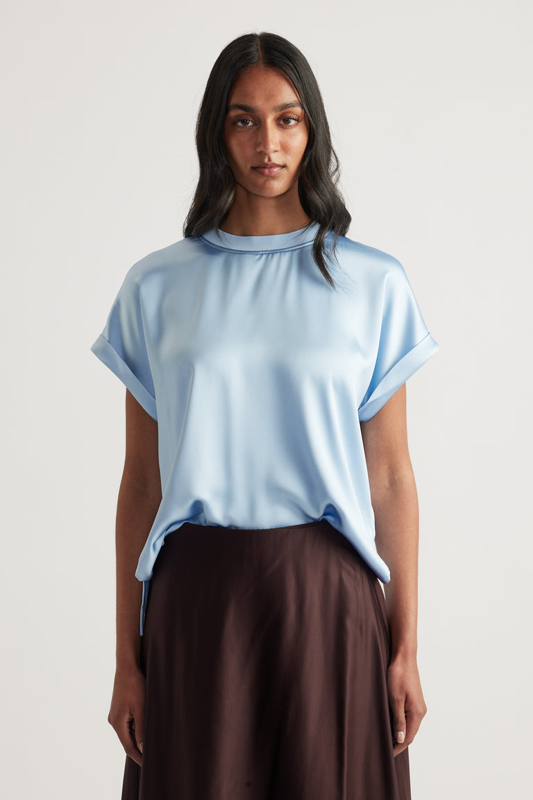 Model wearing a light blue satin tee with short sleeves and dark brown pants