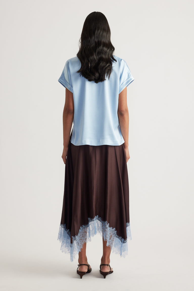 Woman viewed from behind wearing a light blue satin tee with a dark lace hem skirt and black heels