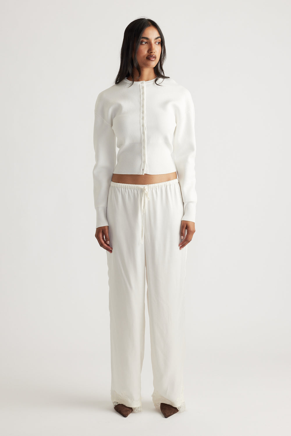 Woman wearing a fitted ivory cardigan with a sleek button front, paired with loose, lightweight drawstring pants for a relaxed look.