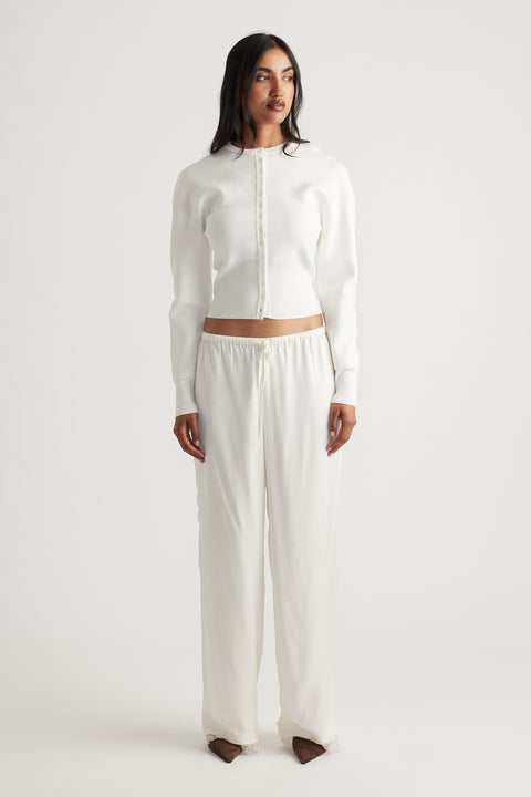 Woman wearing a fitted ivory cardigan with a sleek button front, paired with loose, lightweight drawstring pants for a relaxed look.