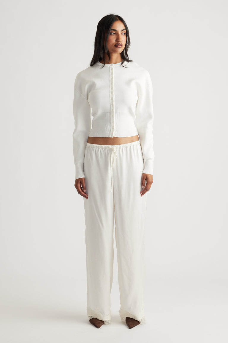 Woman wearing a fitted ivory cardigan with a sleek button front, paired with loose, lightweight drawstring pants for a relaxed look.