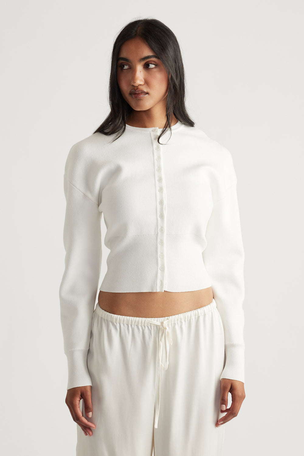 Woman wearing an ivory cinched cardigan with long sleeves, paired with relaxed drawstring pants for a casual look