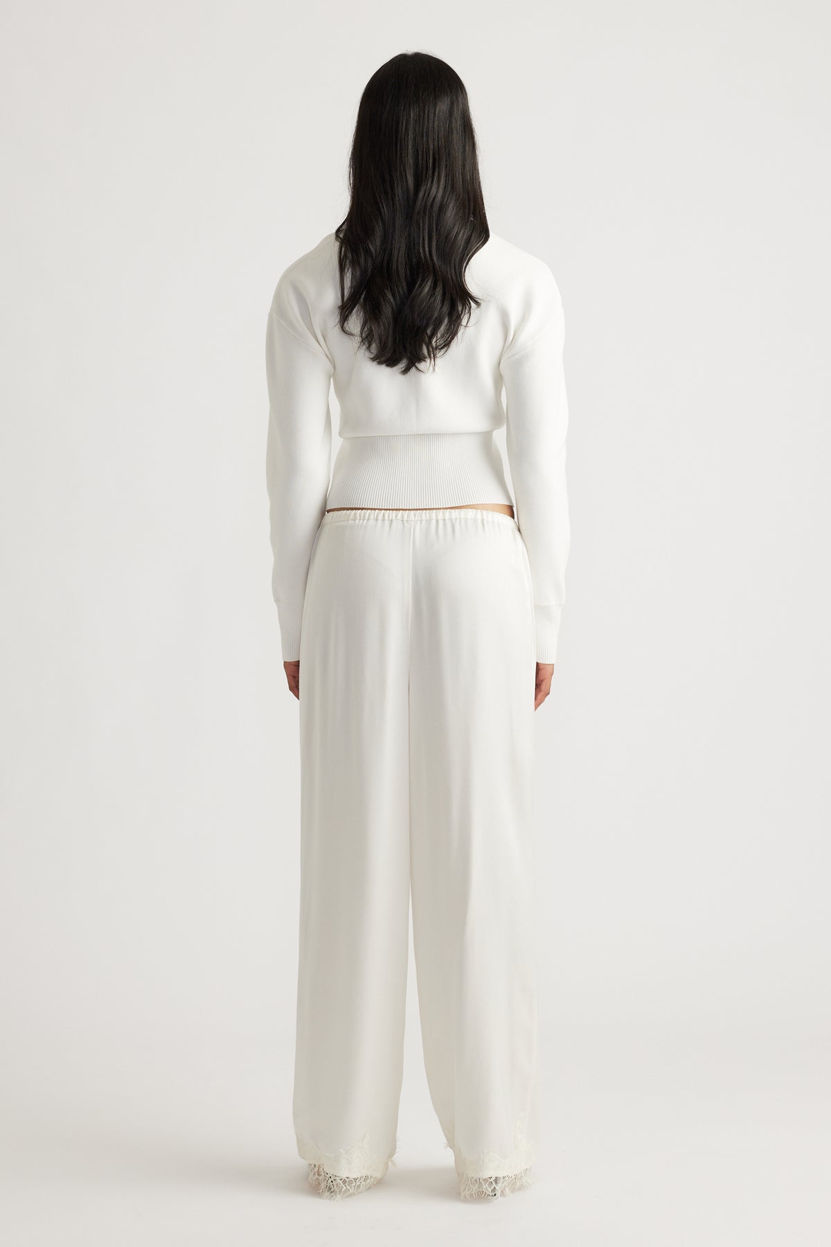 Woman wearing an ivory cinched cardigan paired with loose, wide-leg silk pants featuring lace trim at the hem