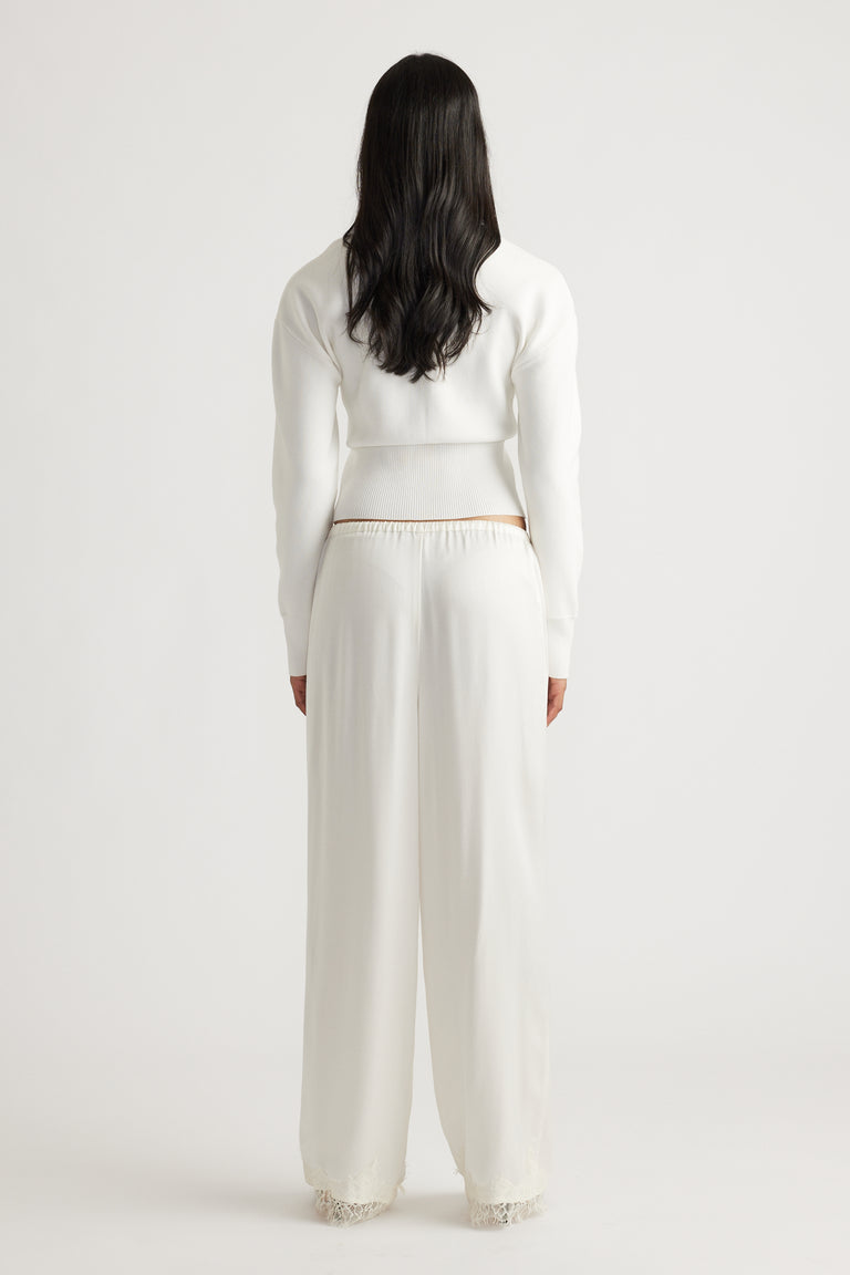 Woman wearing an ivory cinched cardigan paired with loose, wide-leg silk pants featuring lace trim at the hem